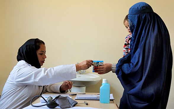 A female doctor gives a woman holding a baby a packet of medicine. 