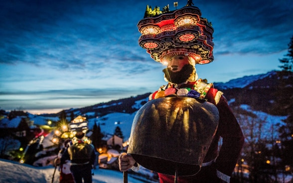 Hombres disfrazados con atuendos y máscaras recorren el vespertino paisaje invernal.