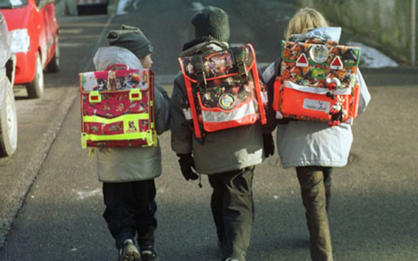 Três crianças com as mochilas a caminho da escola.