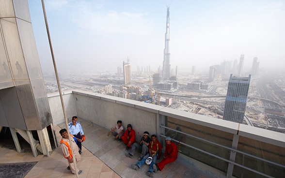 Operai edili fanno una pausa sulla terrazza di un palazzo di Dubai. Nonostante la foschia, sullo sfondo si possono distinguere numerosi grattacieli e la torre Burj Khalifa, l’edificio più alto del mondo. © Piotr Zarobkiewicz