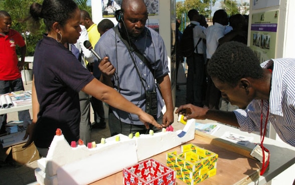 Un ingegnere haitiano impiegato della DSC risponde alle domande di un giornalista davanti a uno stand.