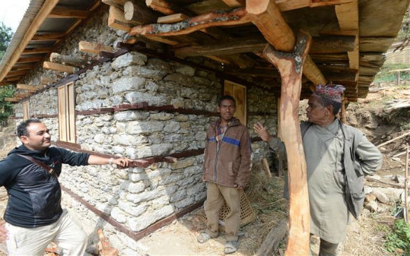 A builder talking with two villagers in front of a rehabilitated house.