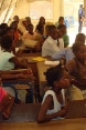 Children sitting at school desks inside a large tent.