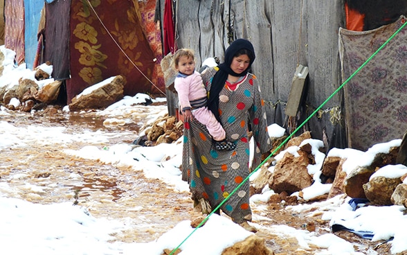 A woman in a Syrian refugee camp holding a child.