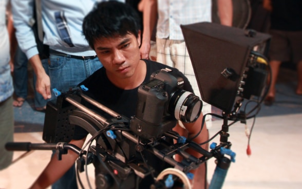 Un giovane regista birmano dietro alla camera da presa, intento a girare un film.