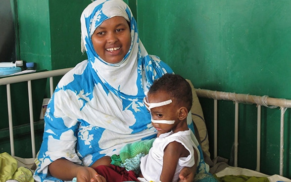 Une femme, assise sur son lit d’hôpital, porte son enfant sur les genoux. Tous deux souffrent de malnutrition sévère. Ils sont soignés dans un hôpital de Mogadiscio, Somalie. 