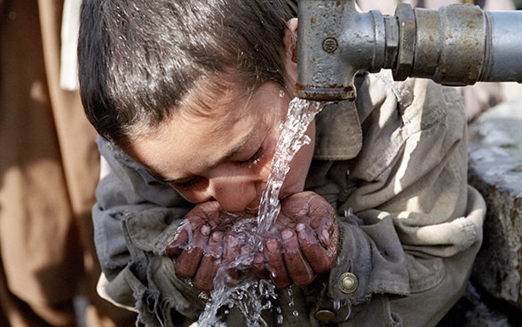 Un ragazzo in Afghanistan beve acqua da una fontana.
