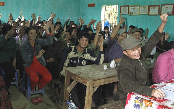 Villagers gathered in a room vote with a show of hands.