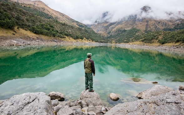 Ein Mann steht an einem See in einer Berglandschaft.