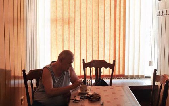 Un homme âgé est assis seul à une table dans une pièce sombre.
