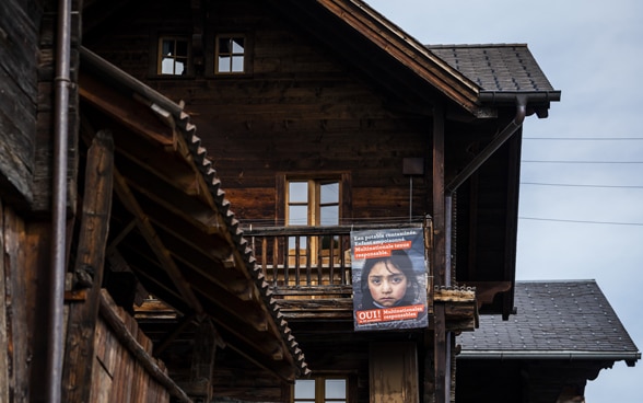 Ein organges Abstimmungsplakat zur «Konzerninitiative» ziert ein altes Berg-Tenn aus dunklem Holz.