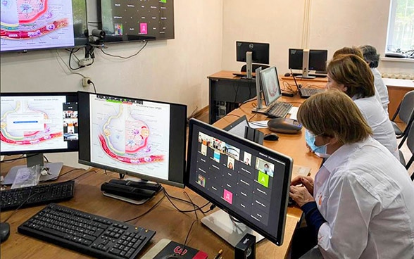 In einem Raum mit vielen Bildschirmen arbeitet das medizinische Personal an Computern.