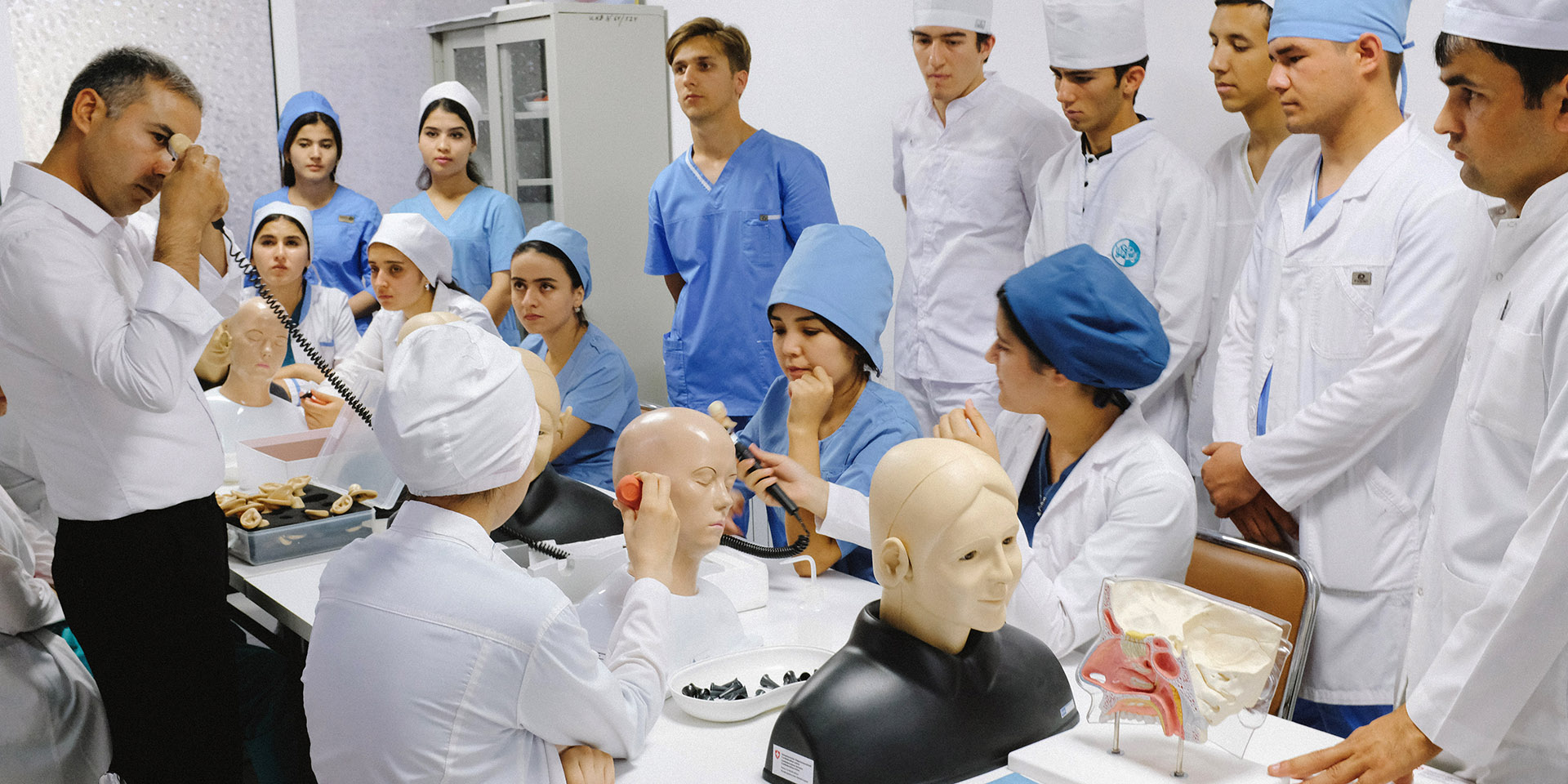 Junge tadschikische Männer und Frauen stehen an einem Tisch. Auf dem Tisch stehen Kunststoffbüsten und medizinische Instrumente zu Ausbildungszwecken. 