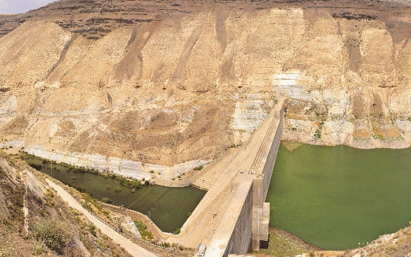 Water flows on both sides of a dam, which stands between two mountain slopes.