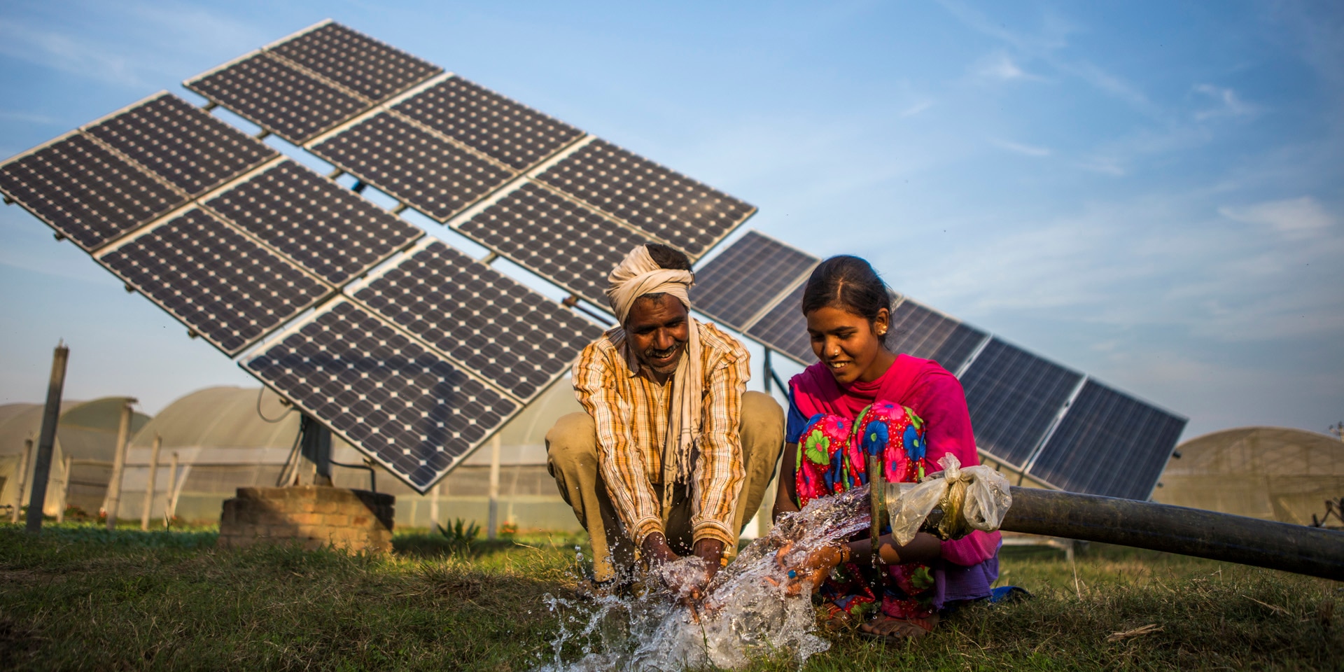 Un hombre y una mujer del Sur con una manguera de agua y paneles solares al fondo.