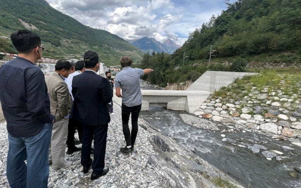 A gesti, uno dei partecipanti dà spiegazioni alle delegazioni asiatiche nelle vicinanze di una diga.