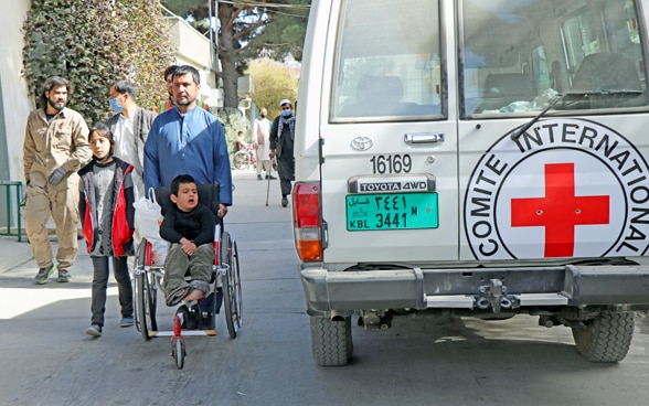 Visitors to an Afghan hospital walk past an ICRC vehicle.