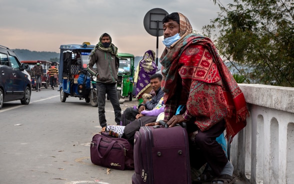 On the side of a road, Nepalese people with their suitcases are preparing to migrate to India.
