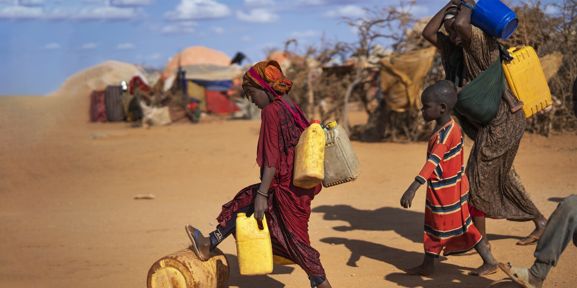 Mujeres y niños transportan bidones de agua a través de una aldea con chozas en Somalia.