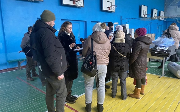 Una mujer habla con personas que llegan a un pabellón deportivo convertido en un refugio de emergencia.