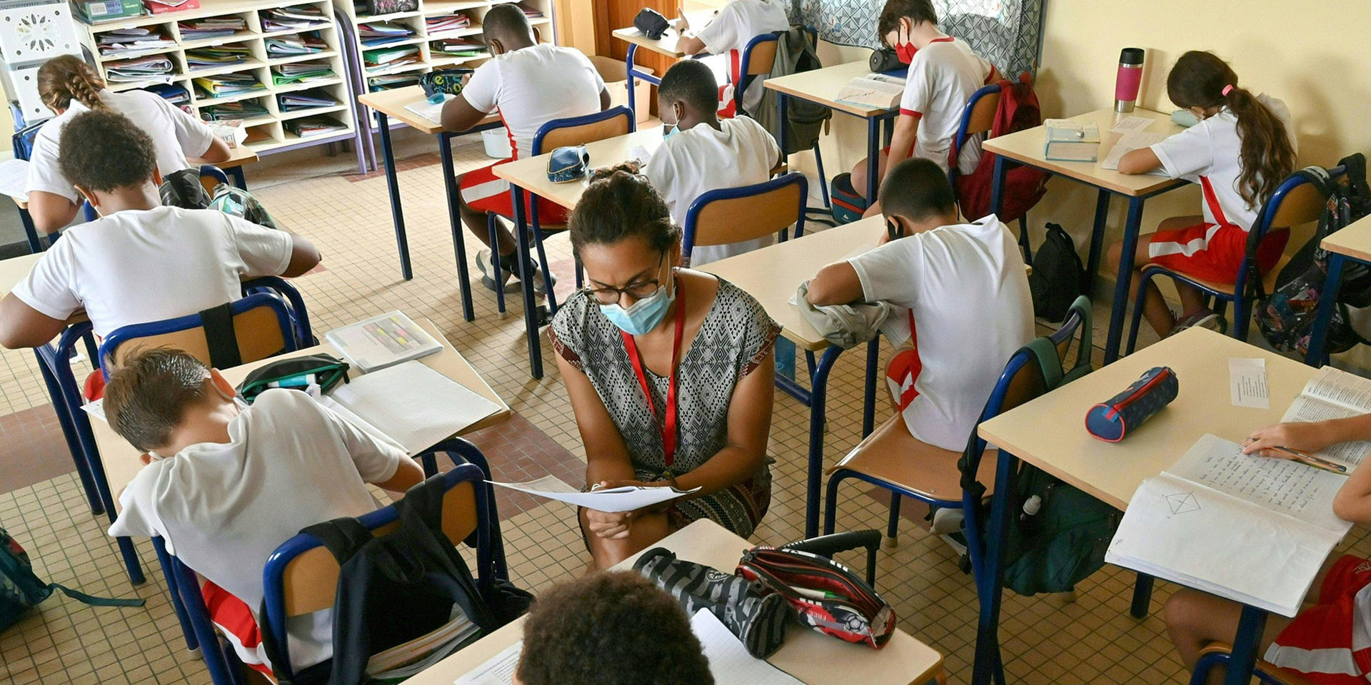 Les enfants sont assis à leur pupitre. L'enseignante les aide à faire leurs devoirs.