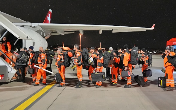 About ten members of Swiss Rescue standing in front of the stairs to the plane.