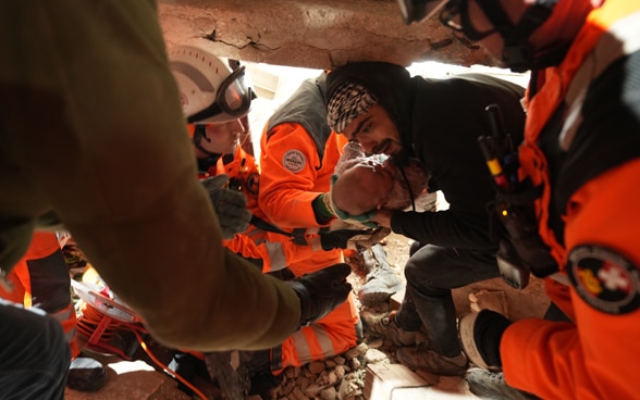  Un uomo, circondato dai membri della Catena di salvataggio, tiene tra le mani una bambina di quattro mesi appena salvata.