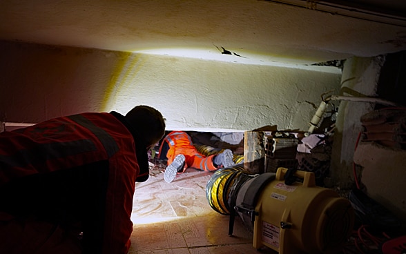 A member of the rescue chain crawls under rubble of a house. A spotlight gives him light.