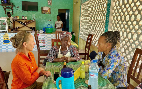 DEZA-Direktorin Patricia Danzi und eine Kollegin vom Schweizer Kooperationsbüro in Benin sprechen in ihrem Lokal mit einer beninischen Gastwirtin.