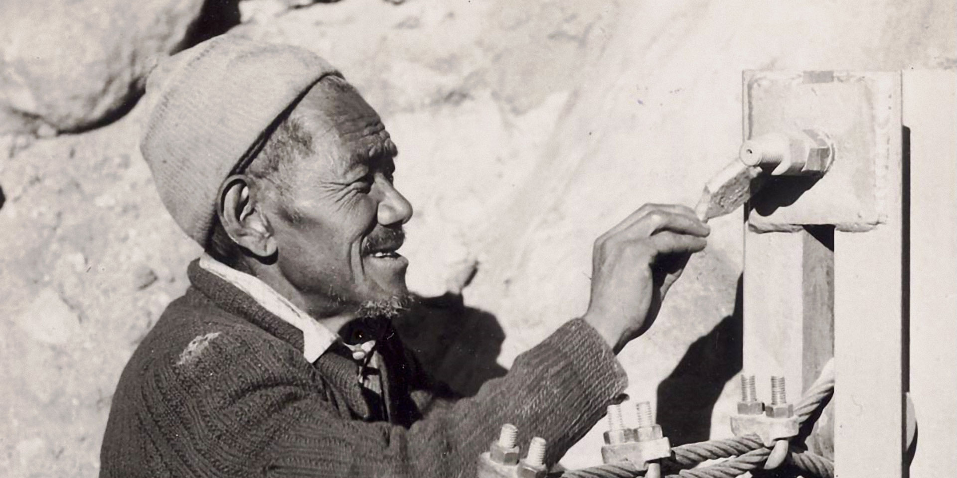 Il nepalese Ang Tsering Sherpa dipinge con vernice e pennello un elemento del ponte.