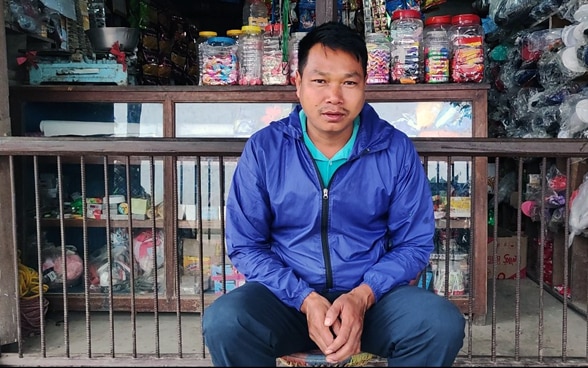 Un commerçant est assis devant son magasin.