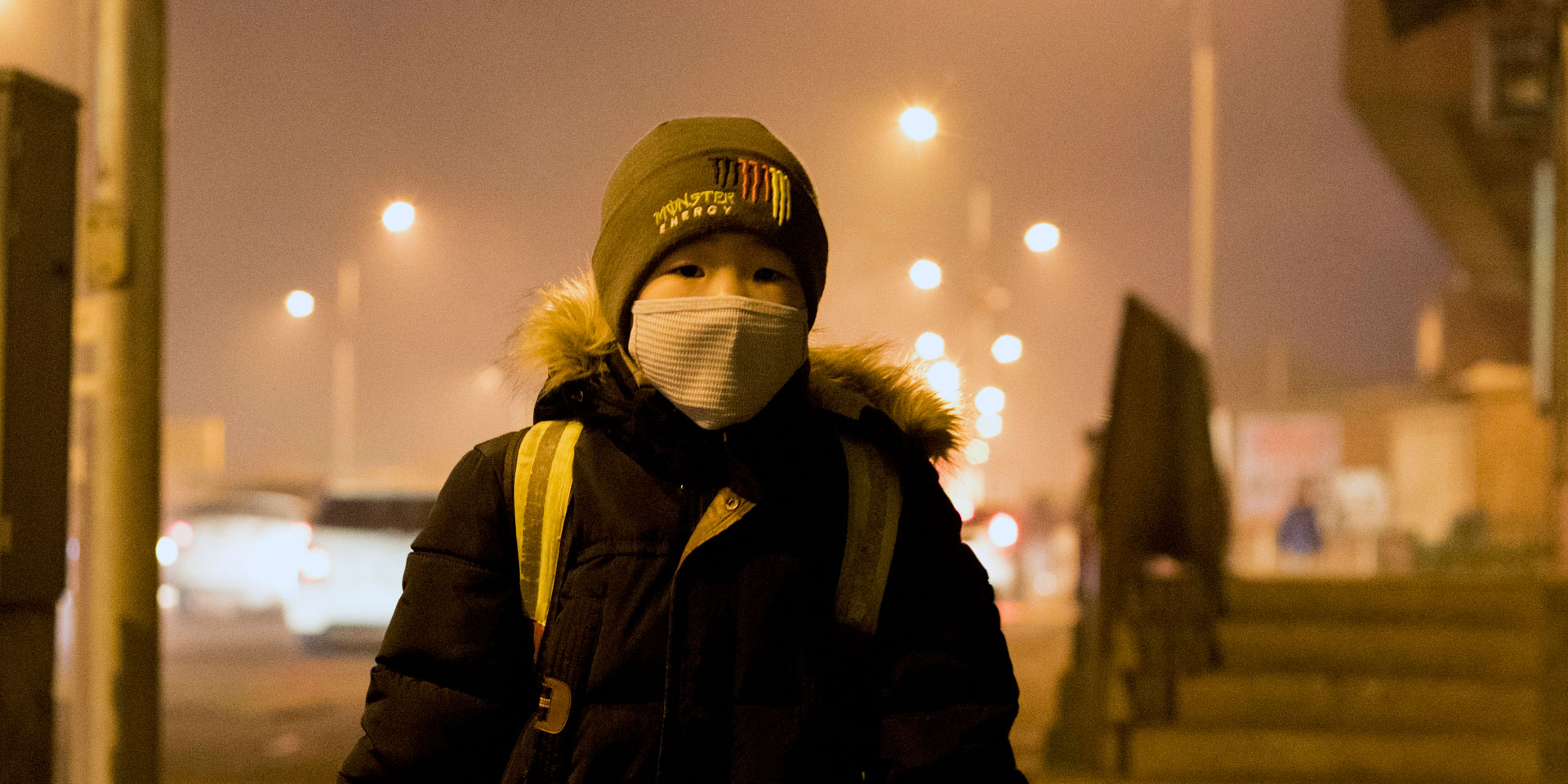 Un garçon portant un cartable et un masque de protection respiratoire attend à un arrêt de bus à Oulan-Bator.