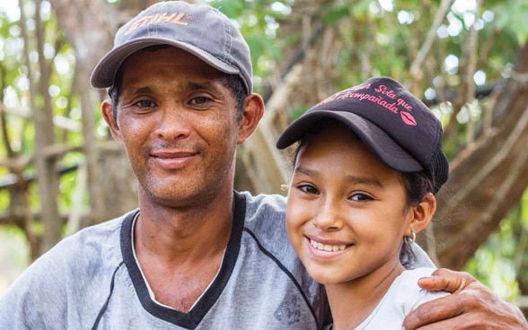 Un père et sa fille rient face à la caméra.