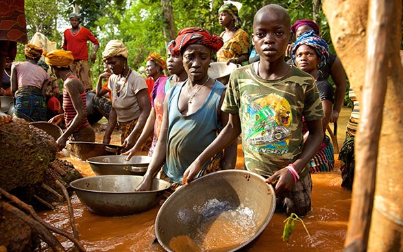 En la foto pueden verse mujeres, hombres y niños de un pueblo de Sierra Leona parados y con el agua hasta la cintura en una mina de oro, intentando limpiar de impurezas el oro extraído.