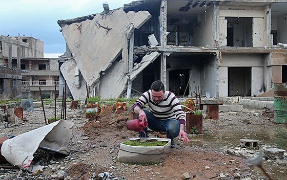 Un uomo sta innaffiando il suo piccolo giardino  nel mezzo della guerra in Siria.