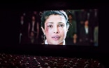 A woman on a cinema screen. Her right cheekbone is scraped and bruised and she is crying.