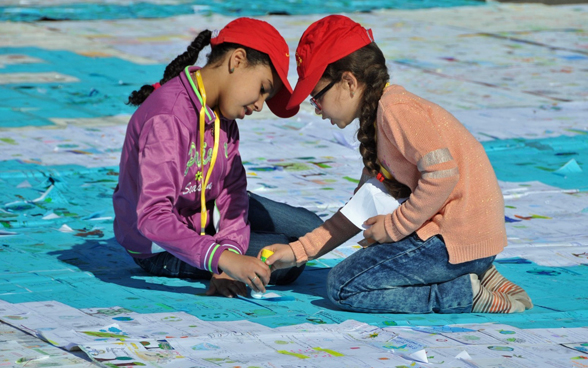 Zwei marokkanische Mädchen kleben auf dem Boden kniend Karten mit einem Leimstift an