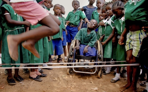 Group of Nigerian schoolchildren skipping rope while a smiling child in a wheelchair looks on.