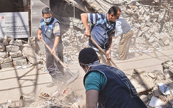 Drei Männer schaufeln in Syrien Steine und Einsturzmasse zusammen. 