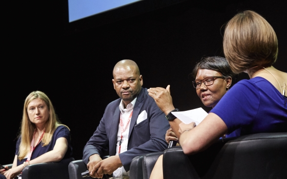 Andrea Heinzer, Sithole Mbanga, Malijeng Ngqaleni und Melanie Pfändler sitzen auf der Bühne. Malijeng Ngqaleni spricht in ihr Mikrophon.