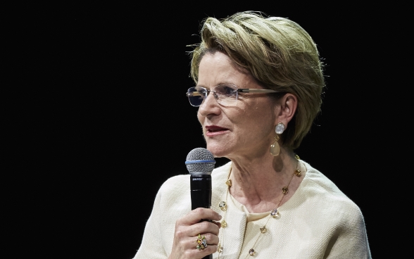 Marie-Gabrielle Ineichen-Fleisch est assise sur la scène et parle dans son microphone. 