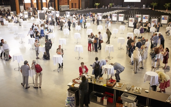 La Festhalle de Bernexpo vue du haut. Des participants éparpillés à de nombreuses tables, s’entretiennent, boivent ou mangent quelque chose.