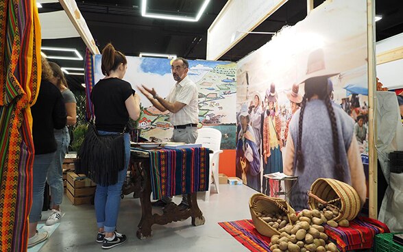 An SDC employee chats to a young woman against a backdrop depicting life in Peru.