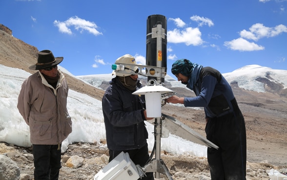 Trois hommes installent une station météorologique automatique dans les hauts-plateaux péruviens. 