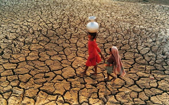 Due bambini con una brocca d'acqua camminano attraverso il letto di un fiume prosciugato.