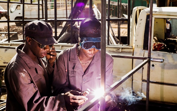 A man instructs a woman to use a welding device.