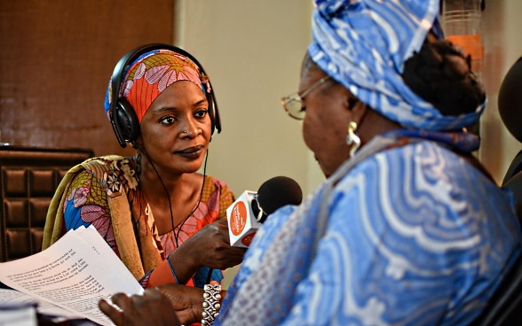 Une femme africaine tend son micro une autre femme dans un studio radio.