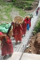 Women carrying baskets walk on a trail bridge.
