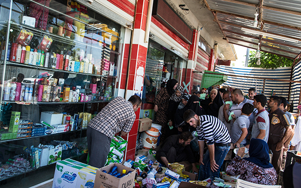 Aid recipients in Iraq queuing outside a supermarket at a point of distribution for food and other goods.