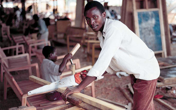 Un joven sierra una tabla de madera.